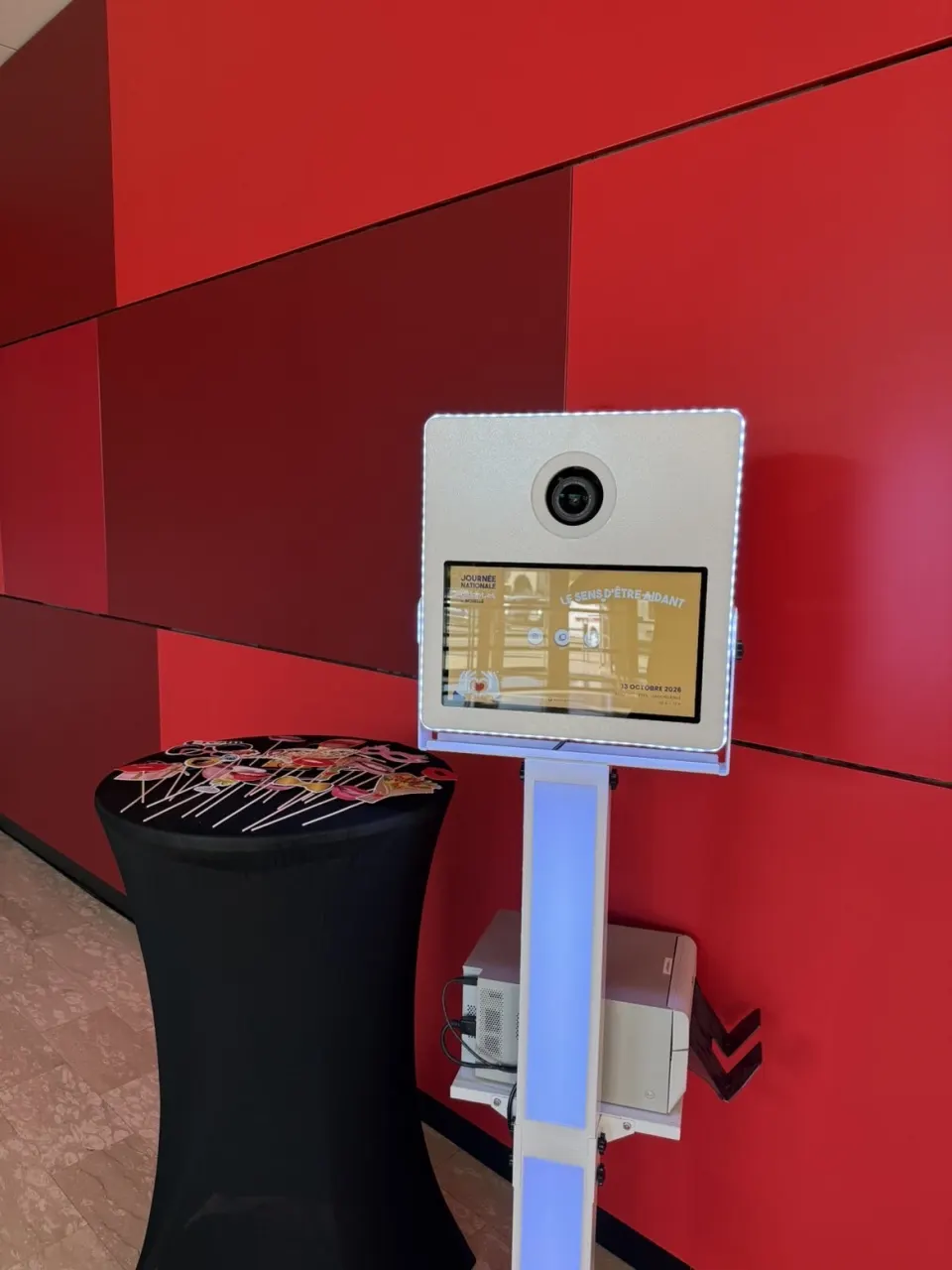 Borne photobooth lumineuse dans une salle des fêtes, écran d'accueil personnalisé pour un évènement de collectivité, accessoires sur un mange-debout