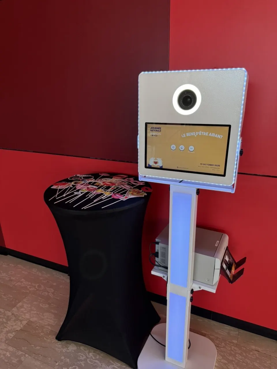 Borne lumineuse installée pour un évènement de collectivité : écran d'accueil personnalisé, accessoires sur un mange-debout, tirage dans le bac de l'imprimante