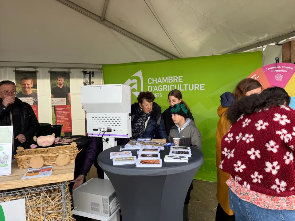 Le stand de la Chambre d'agriculture des Vosges sous la tente : grand fond vert, borne vue de dos, mange-debout garni de brochures