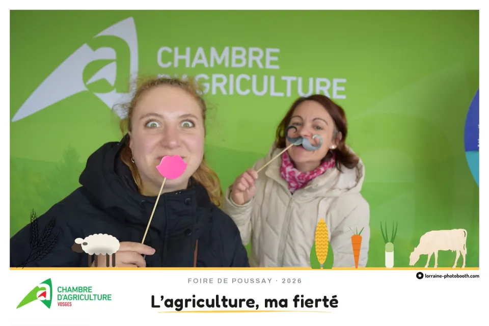 Tirage de la Foire de Poussay : deux visiteuses posent avec une bouche et une moustache en carton, slogan « L'agriculture, ma fierté »