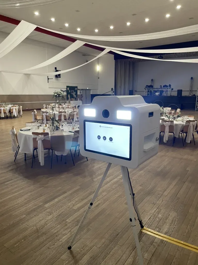 Borne photobooth sur trépied installée dans une salle de mariage dressée, trépied posé devant les tables