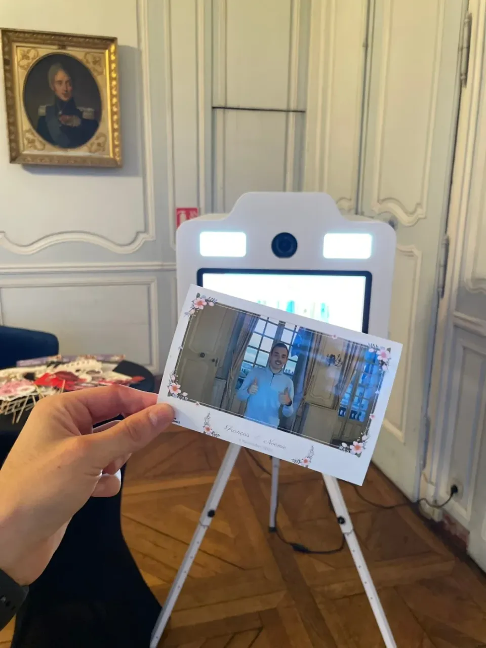 Tirage 10x15 au cadre fleuri « François & Noémie », tenu devant la borne