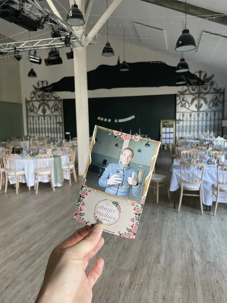 Tirage 10×15 au cadre fleuri des mariés, tenu à la main dans la salle de réception dressée